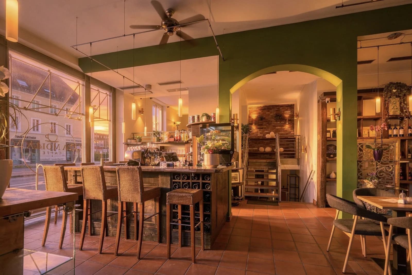 Bar mit Siebträgermaschine, olivgrüne Wand und Terrakottaboden im Abendlicht